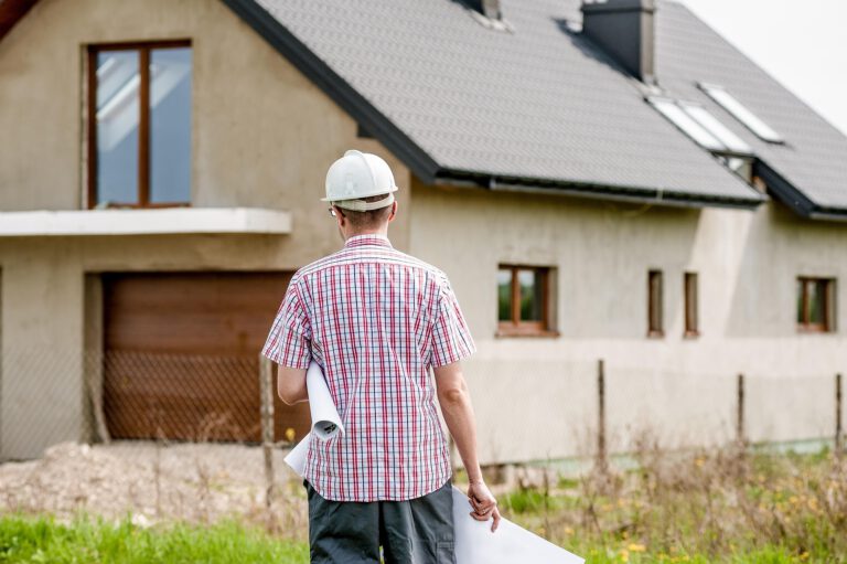 Bauleiter mit Helm und Bauplan vor einem Neubau