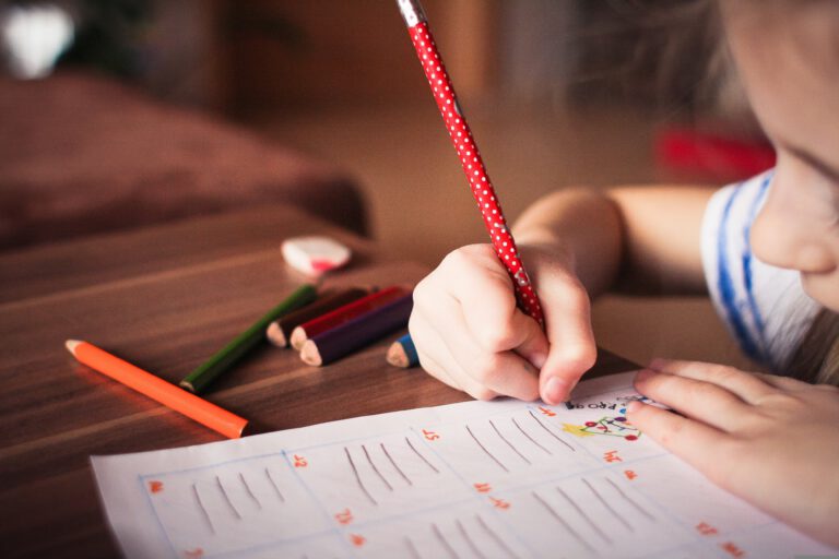 Kind schreibt mit Buntstiften in ein Schulheft